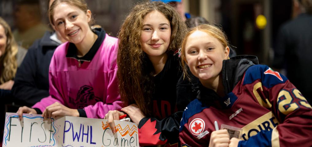 Fans wait for PWHL players to arrive at Scotiabank Centre with handmade signs to cheer them on